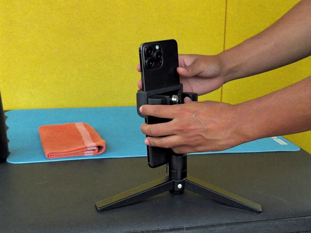 Hands securing a phone in a compact tripod at the gym